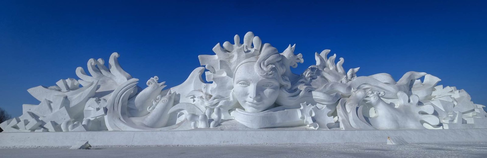 A massive snow sculpture with a woman's face in the center surrounded by chickens
